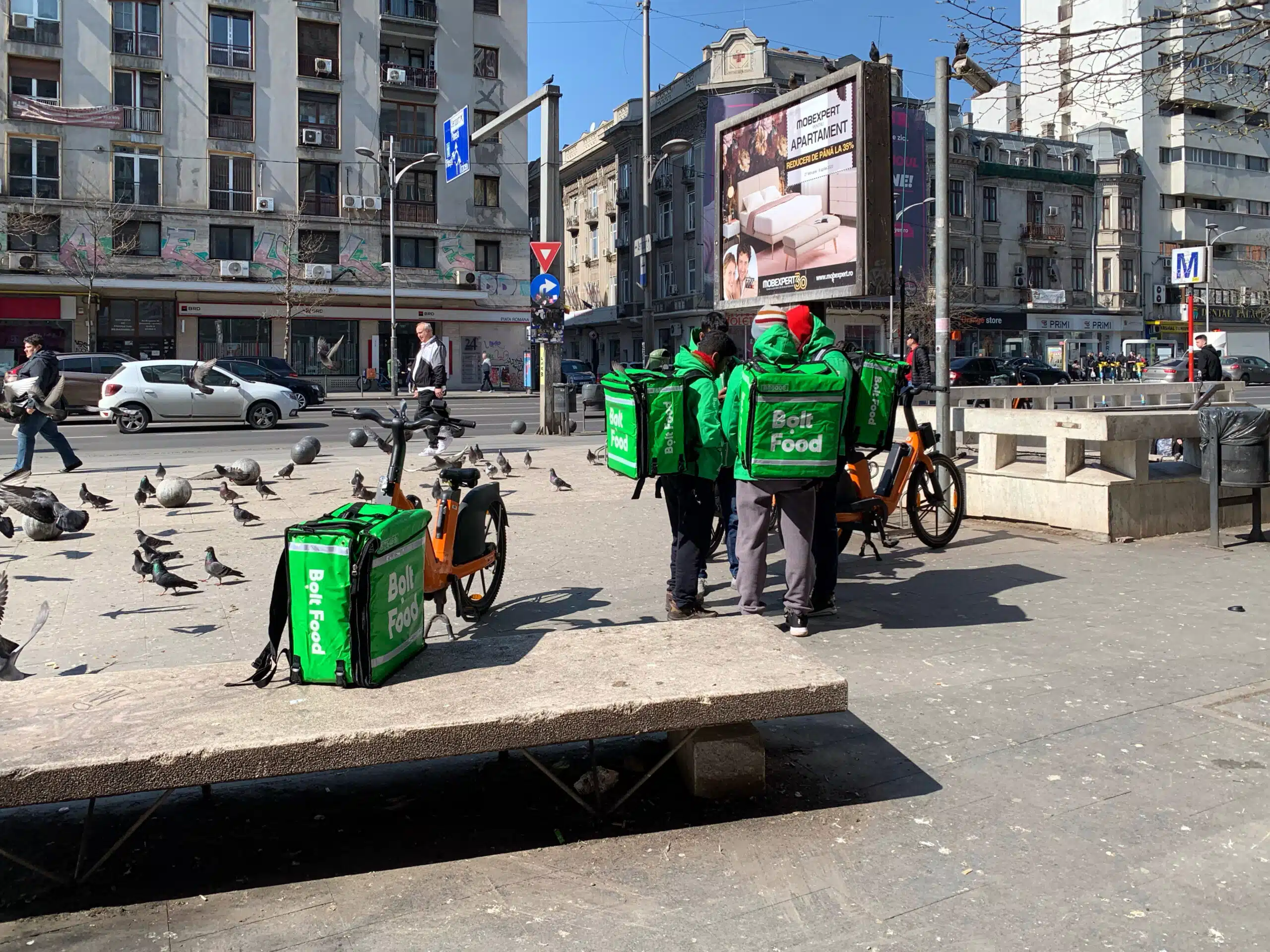 Food delivery riders feeding pigeons at Piața Romană, Bucharest (2023)